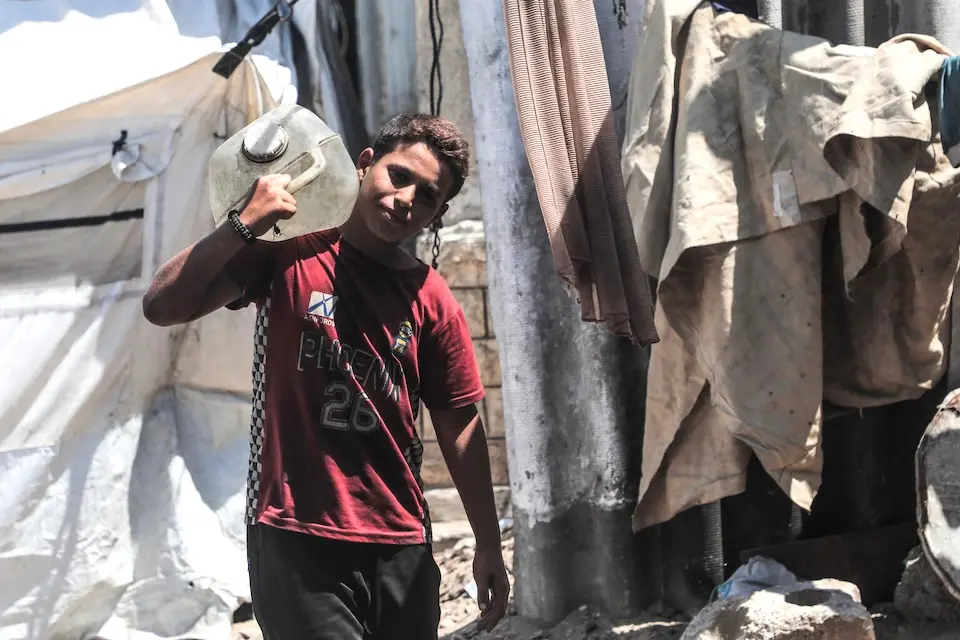 Hassan, 12, carries a container of water on his shoulder in Gaza.
