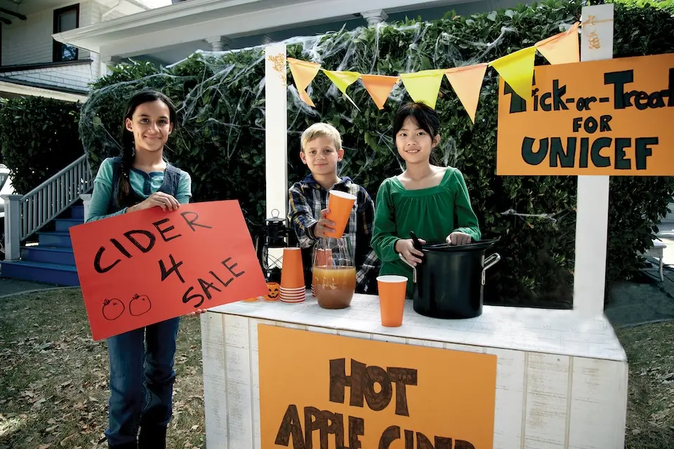 Kids trick-or-treating for UNICEF run a stand serving hot apple cider.