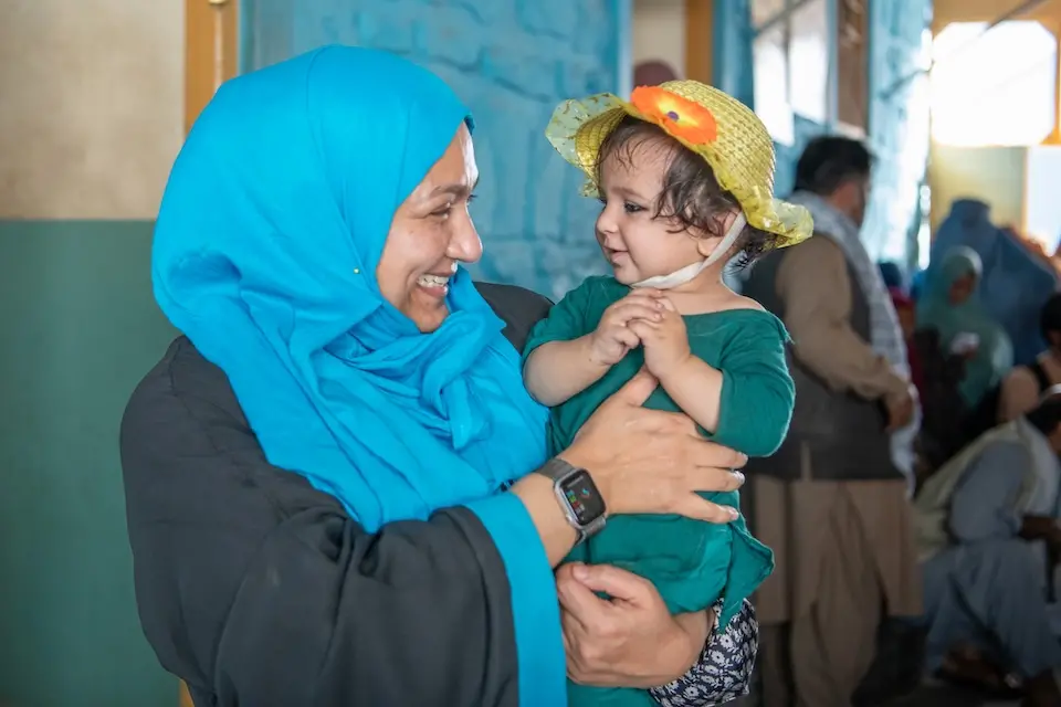 Woman wearing head covering holding young girl and smiling at her
