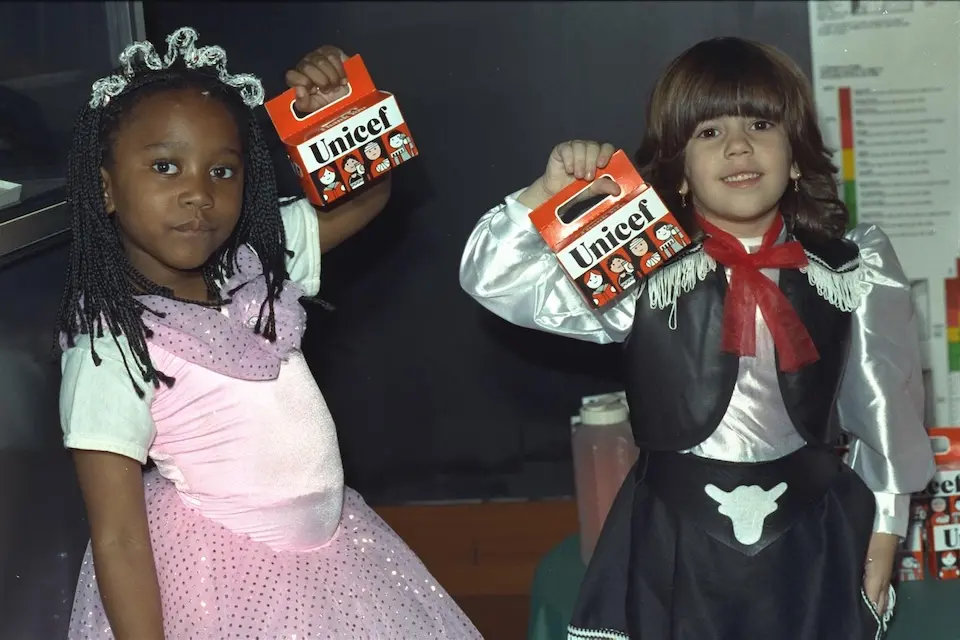 Two young girls in costume hold up Trick-or-Treat for UNICEF collection boxes.
