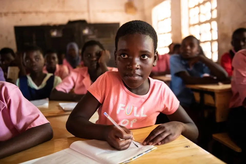 Miracle writes while seated at her new desk from the K.I.N.D. Fund at Bwengu Primary School in Malawi in 2024.