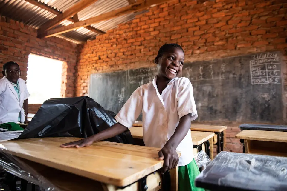 A girl smiles while unwrapping a new desk from the K.I.N.D. Fund at Vizara Primary School in Malawi in 2024.