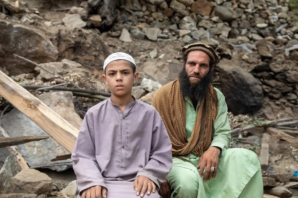 An 11-year-old boy and his father sit in the ruins of their home, destroyed by an earthquake in Kunar province, Afghanistan. 