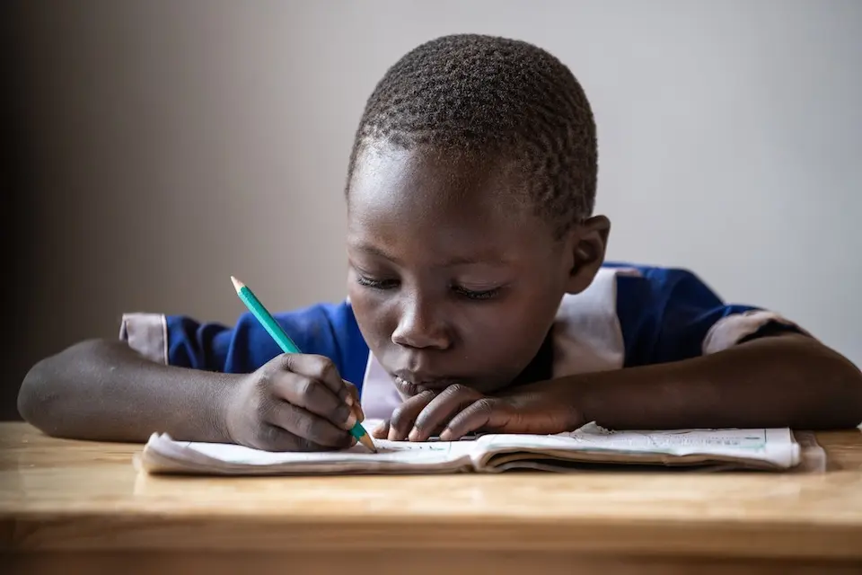 A girl writes in a notebook on her desk in a classroom in Malawi.