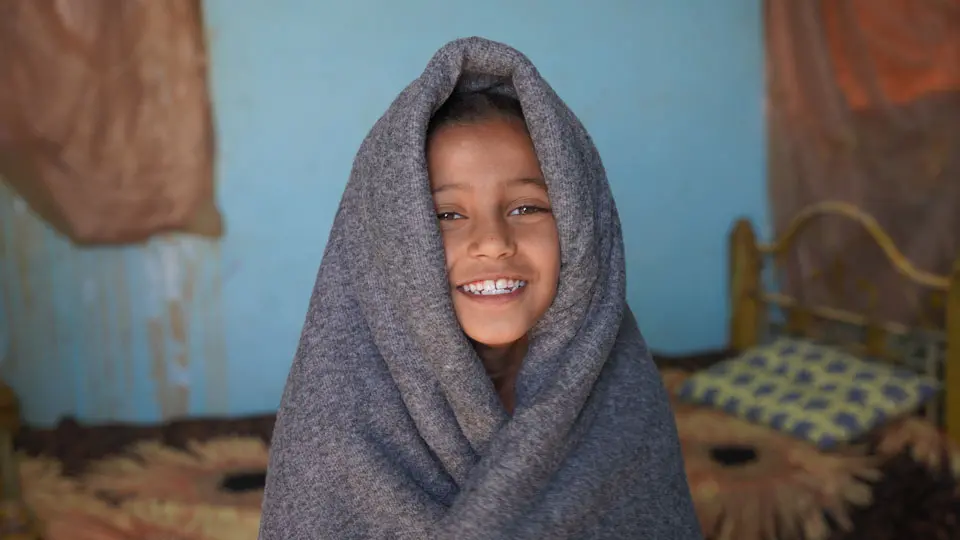 Smiling child wrapping in a blanket received from UNICEF