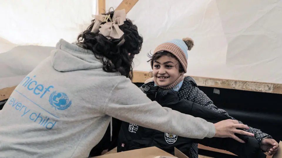 Smiling child checking if a winter coat fits with help from a UNICEF worker
