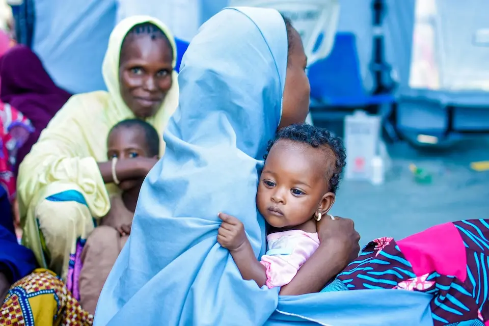 A mother brings her child for treatment at a UNICEF-supported health center in Nigeria following floods