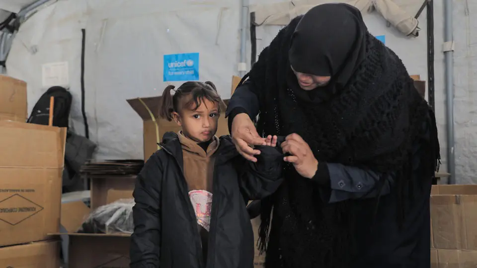 Mother and child trying on a winter coat in a UNICEF tent