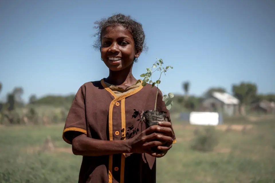 A 4th-grade student in Madagascar holds a small tree sapling.
