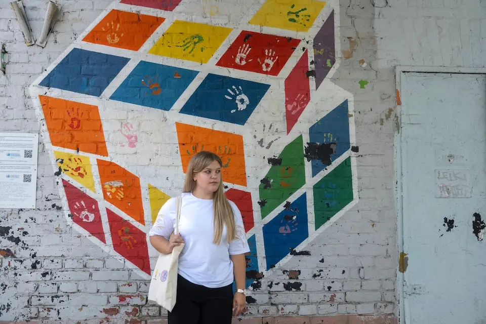A teenager stands in front of a mural painted by children in Kharkiv, Ukraine.