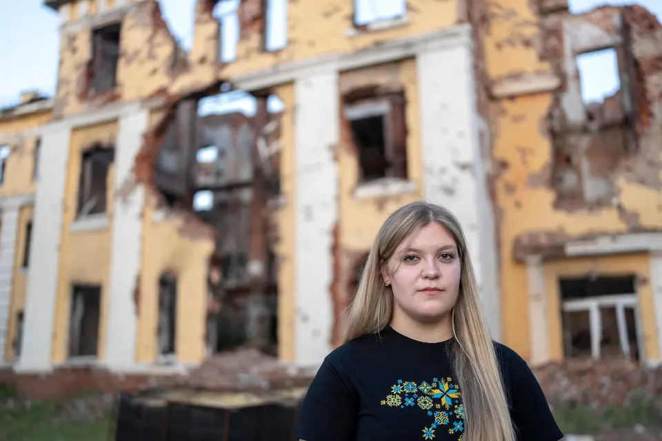 A teenager stands outside the ruins of her former school in Kharkiv, Ukraine.