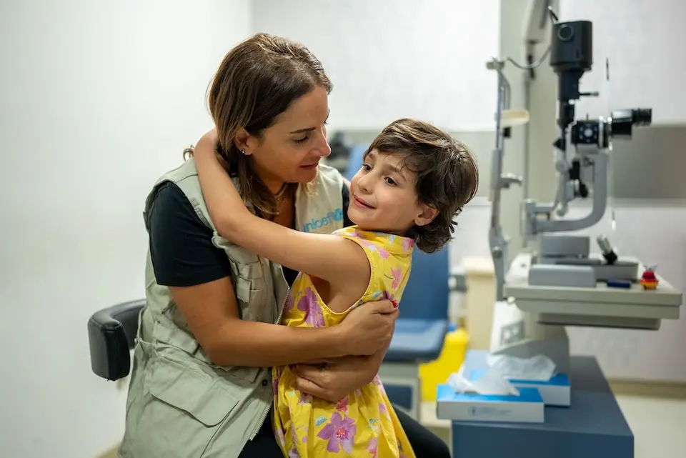 A girl in Lebanon who was injured during conflict embraces a UNICEF staff member at health facility where she received care.