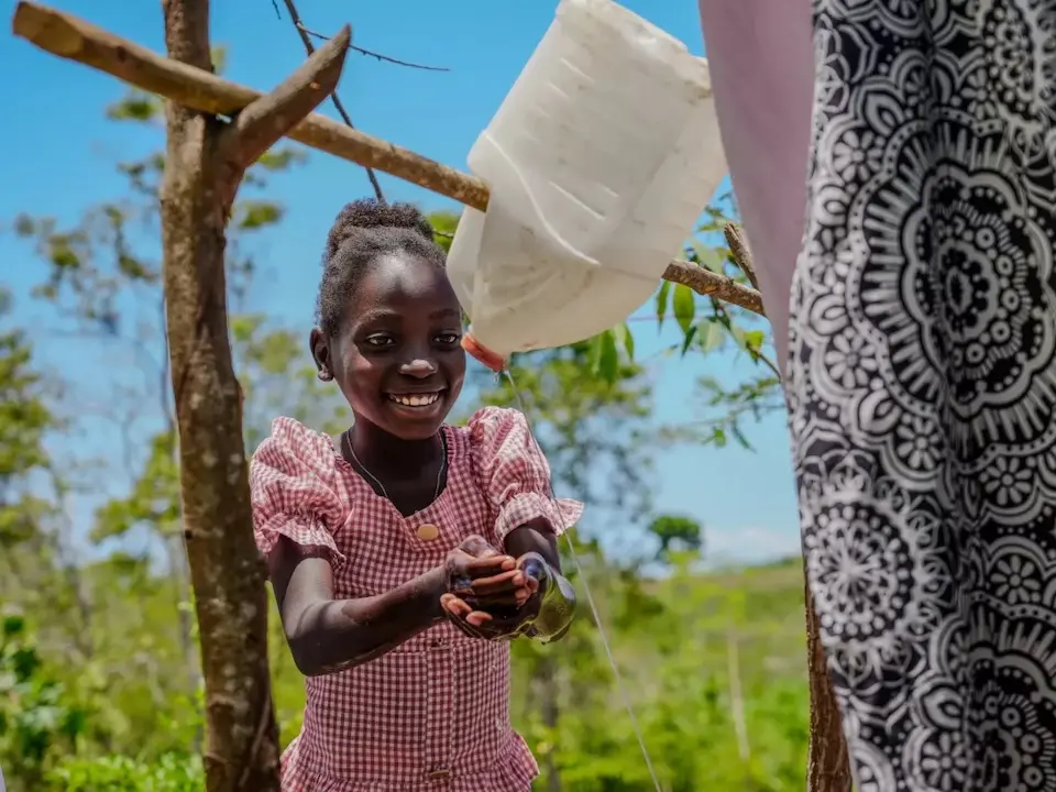 A young girl in Haiti washes hands by the latrine installed as a cholera prevention measure.