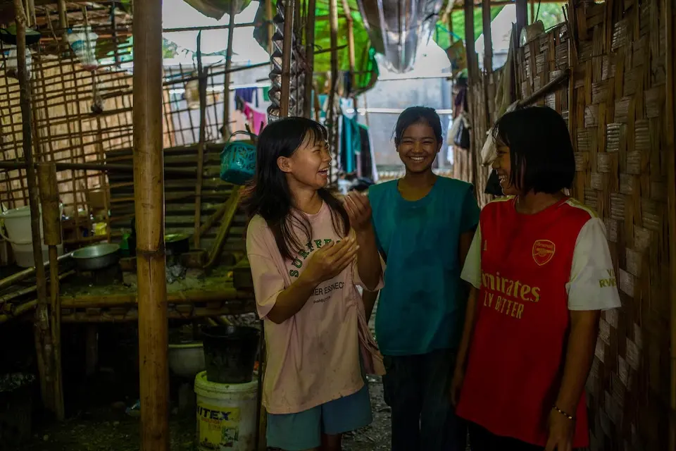 Inside a UNICEF-supported displacement camp in Kachin State, Myanmar, three teenage girls share a laugh while heading to a football game. 