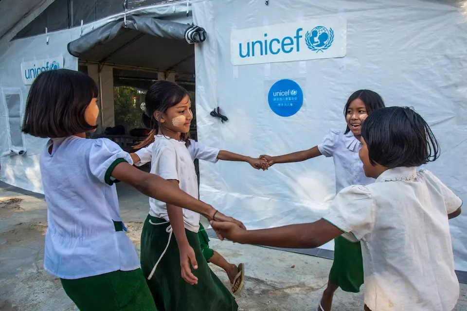 In Mandalay, Myanmar, four students join hands outside a temporary learning space UNICEF provided to address impacts of the March 2025 earthquake.
