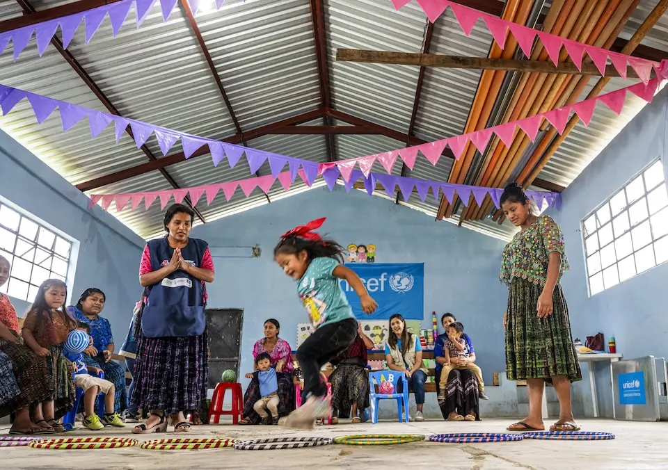 Children play in high-ceilinged room decorated with banners and a UNICEF sign in Guatemala. 