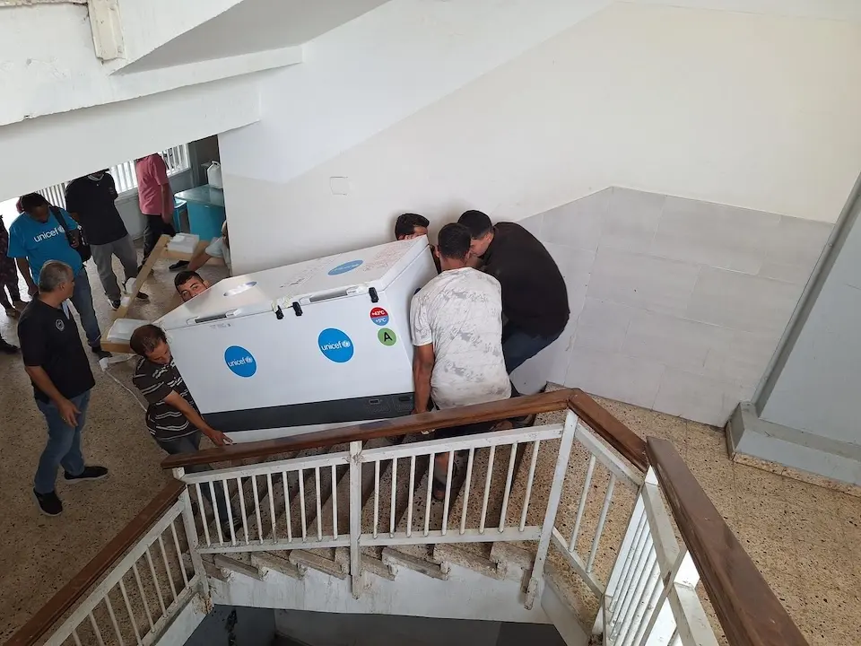 UNICEF staff and partners carry a solar-powered refrigerator up a flight of stairs at a health clinic in Gaza on Nov. 7, 2025.  