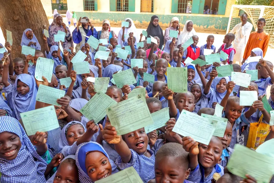 On Nov. 14, 2025, a crowd of happy children hold up their vaccination cards at Sarki Sani Model Primary School in Argungu, Nigeria.