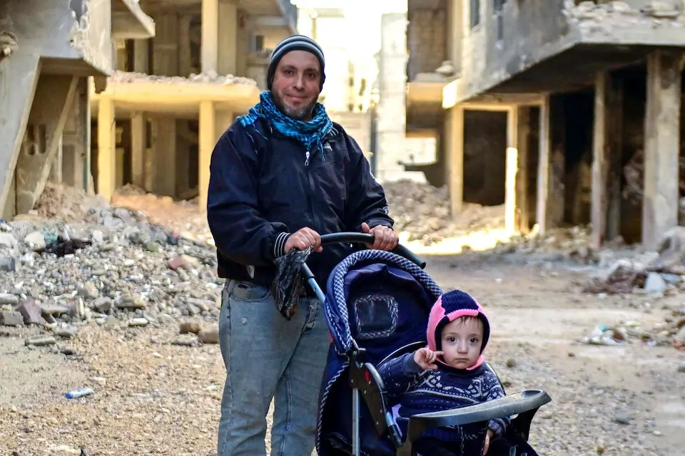 A father pushes his 2-year-old son in a stroller through the damaged streets of Tadamon neighborhood in Damascus, Syria.