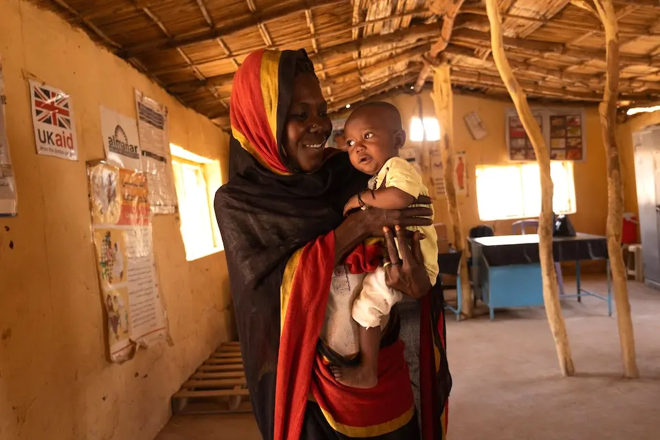 A mother holds her malnourished child, who is being treated for malnutrition at a UNICEF-supported health center in the Mayo area, Jabal Awliya locality, Sudan. 