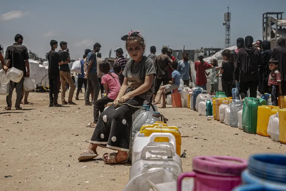 A girl sits in a long queue waiting for a water truck to arrive at her refugee camp in Gaza City, State of Palestine. 