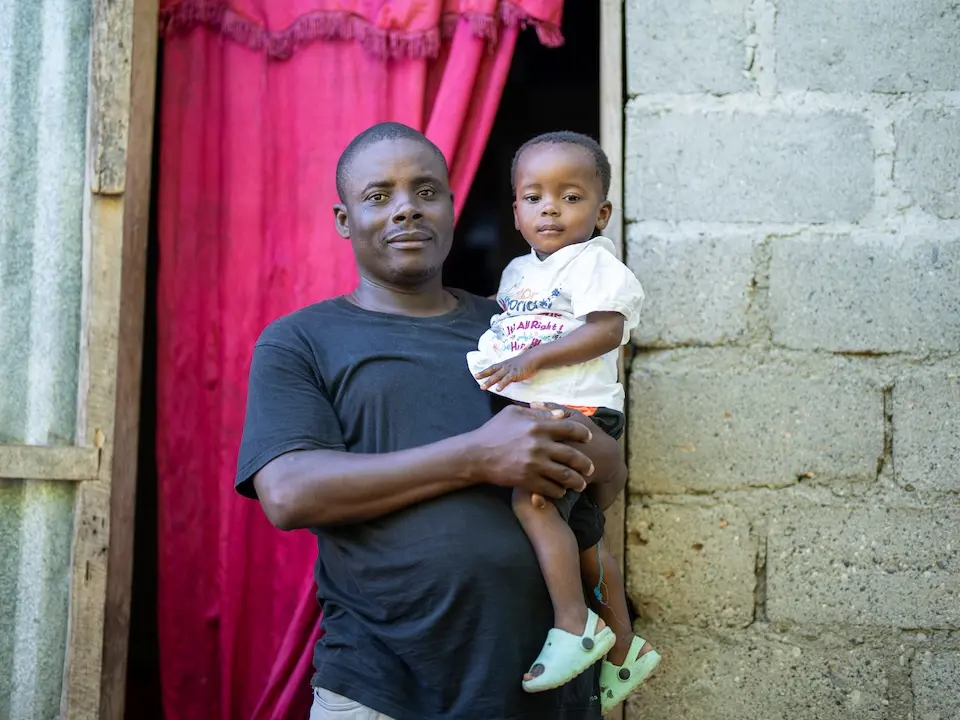 A father and child outside their home in Roseaux commune, Haiti, where UNICEF helped families recovery following Hurricane Melissa.