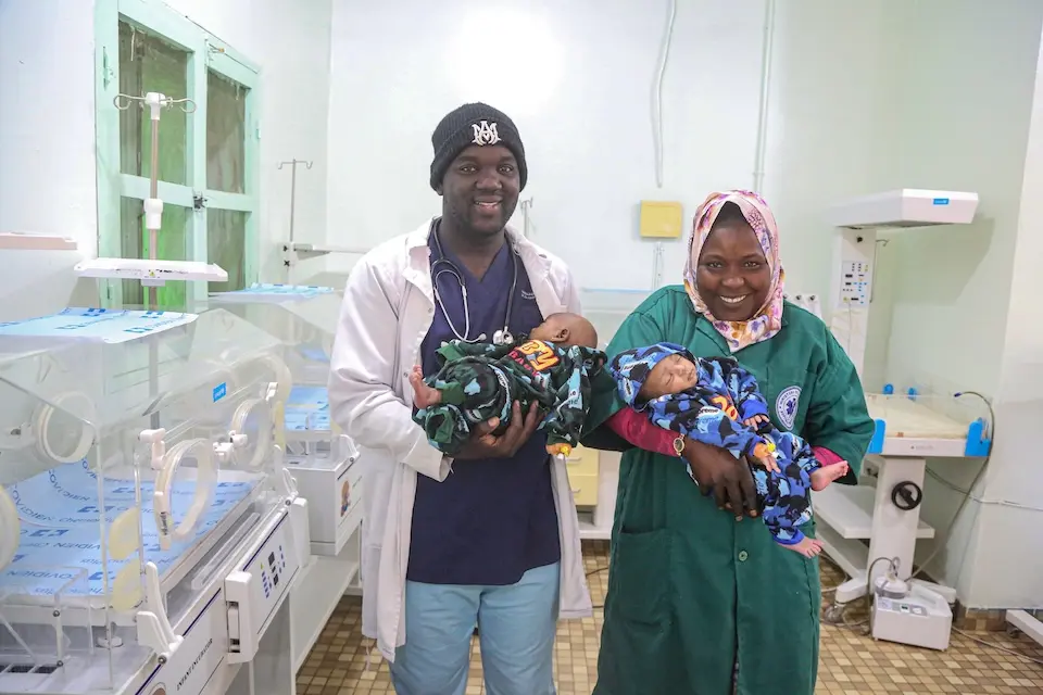 Two health workers cradle newborn twins in the neonatal unit running on solar power in Mali.