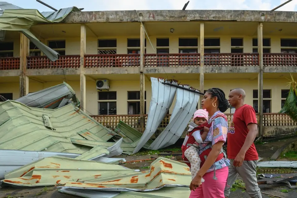 A woman in Madagascar carrying a small child walks past a building damaged by Cyclone Gezani.
