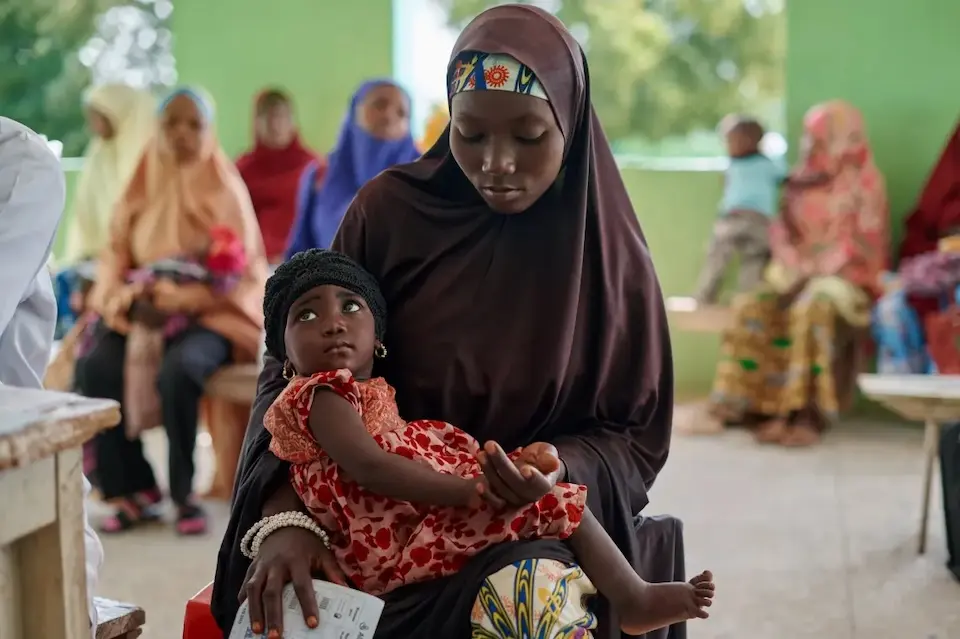In Nigeria at a UNICEF-supported health facility providing vaccinations for children, a mother holds her child in her lap.