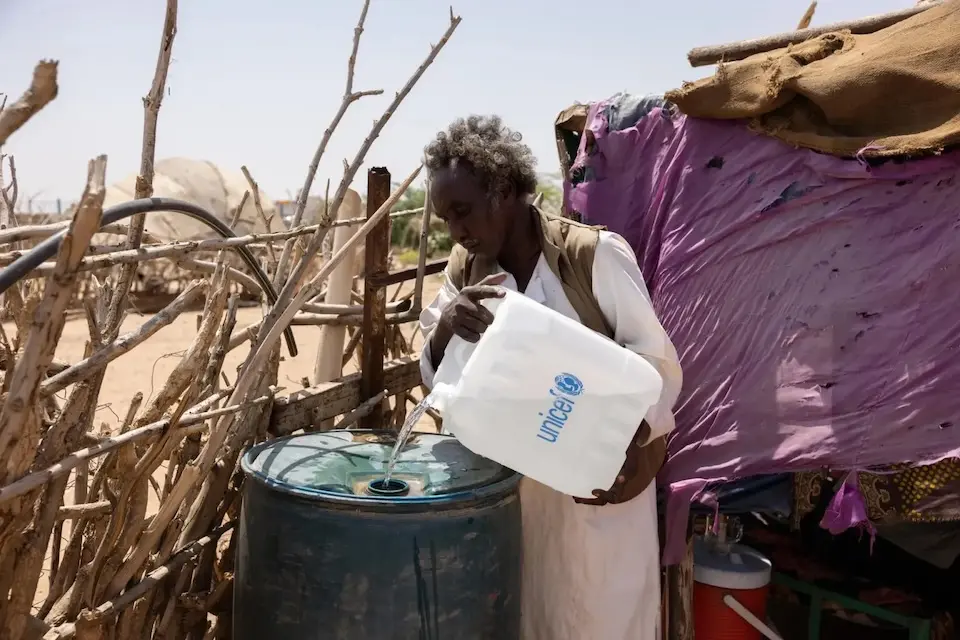 A father pours water from a UNICEF container into a water drum in Sudan's River Nile State.