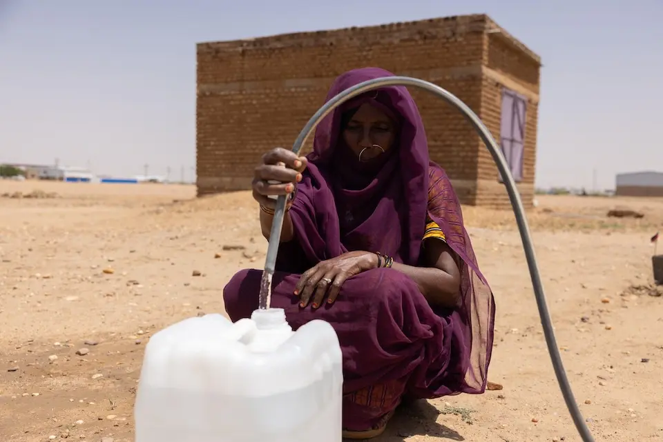 A mother fills a water container from a hose at the back of her house in Aldamer, River Nile State, Sudan.
