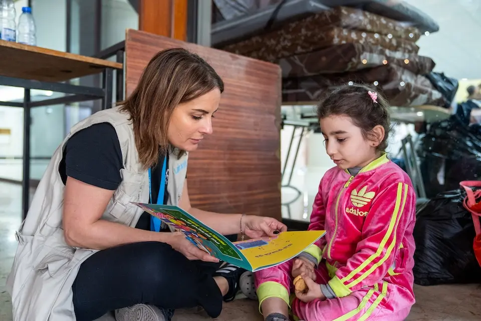 A UNICEF staff member reads a book with a child in Lebanon displaced by escalating conflict.
