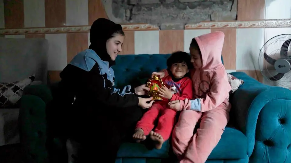 Children sit on a couch and play in their family's home, damaged by conflict in Gaza. 