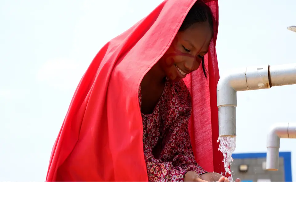 Young woman wearing a red scarf smiling as she holds her hands under a running spigot.