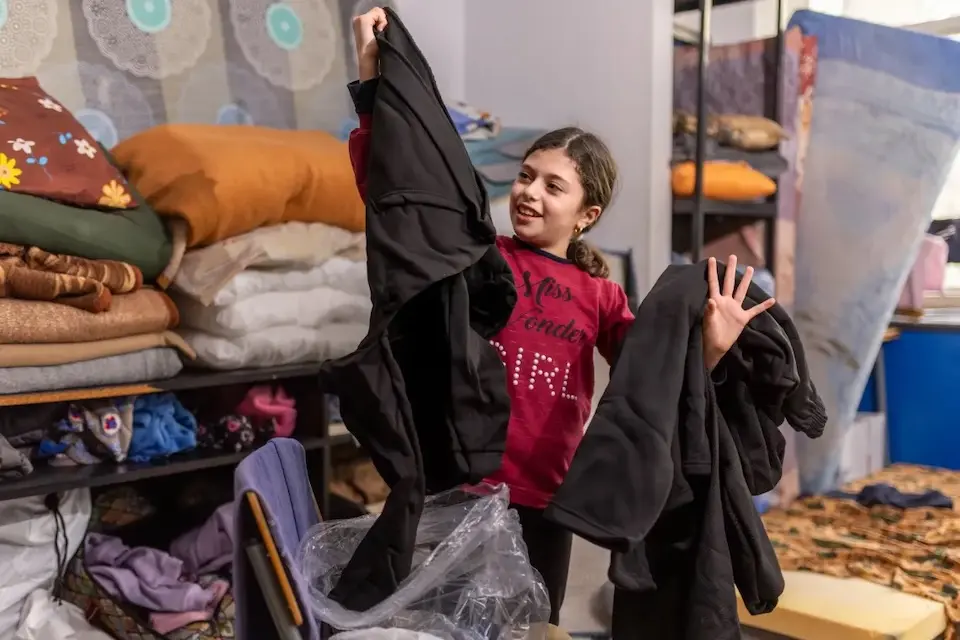 At a displacement center in Lebanon, a child opens a UNICEF winter clothing kit containing items made by young people. 