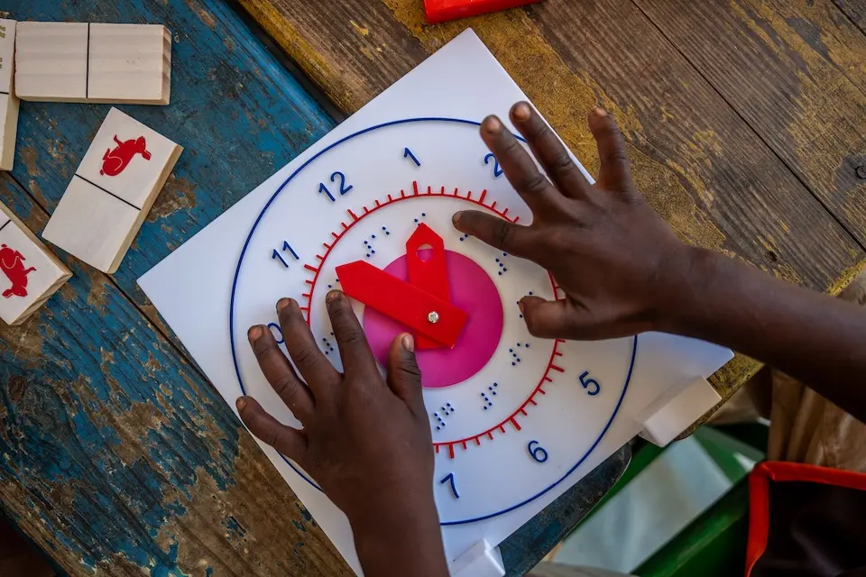 A preschool student in Madagascar engages with the clock provided in each UNICEF School-in-a-Box kit to teach kids how to tell time.