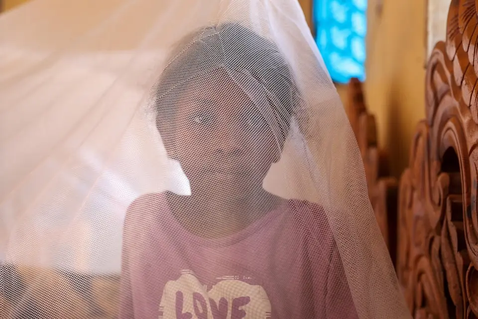 A 10-year-old child in Sudan sits under a mosquito net provided as part of a UNICEF supported program.