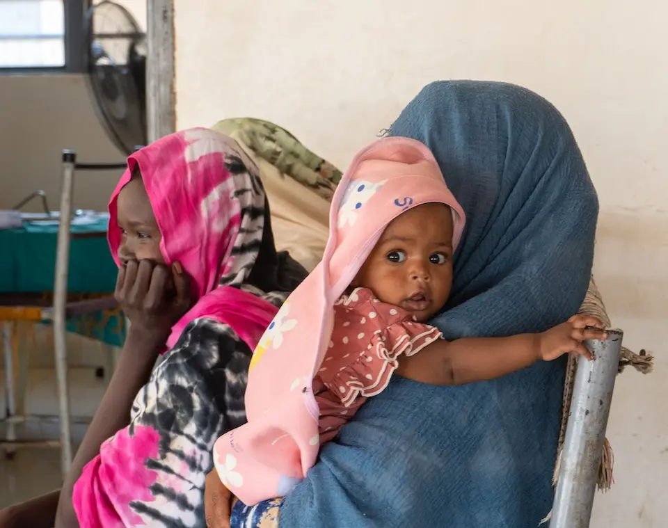 A mother holds her young child awaiting health services at a UNICEF-supported facility in Sudan's White Nile state.
