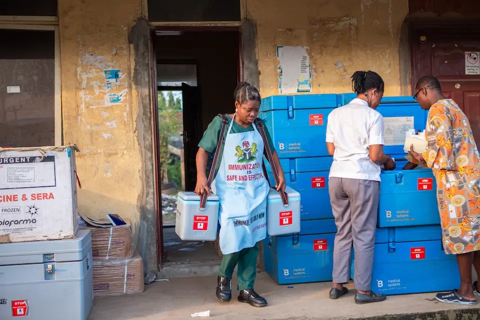 A vaccinator carries vaccine cold boxes outside a primary health care center in Ogun state, Nigeria.