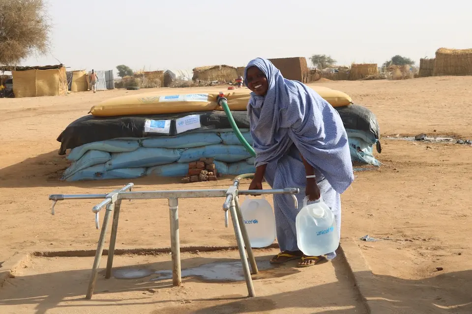 A mother displaced by conflict fills two water containers with safe water from UNICEF distribution point in Tawila, North Darfur, Sudan.
