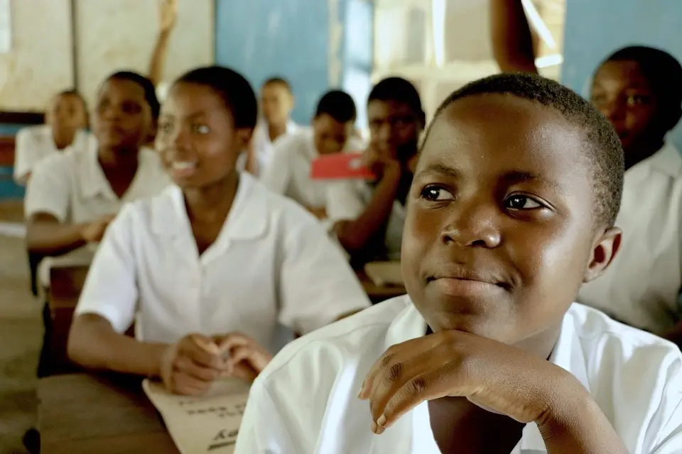 Seated at desks, students listen and raise their hands in a classroom in Malawi in 2017.