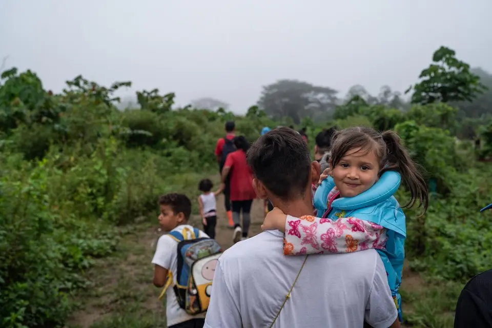 A young girl, carried by her father, shortly after surviving the dangerous migration journey through the Darien Gap.