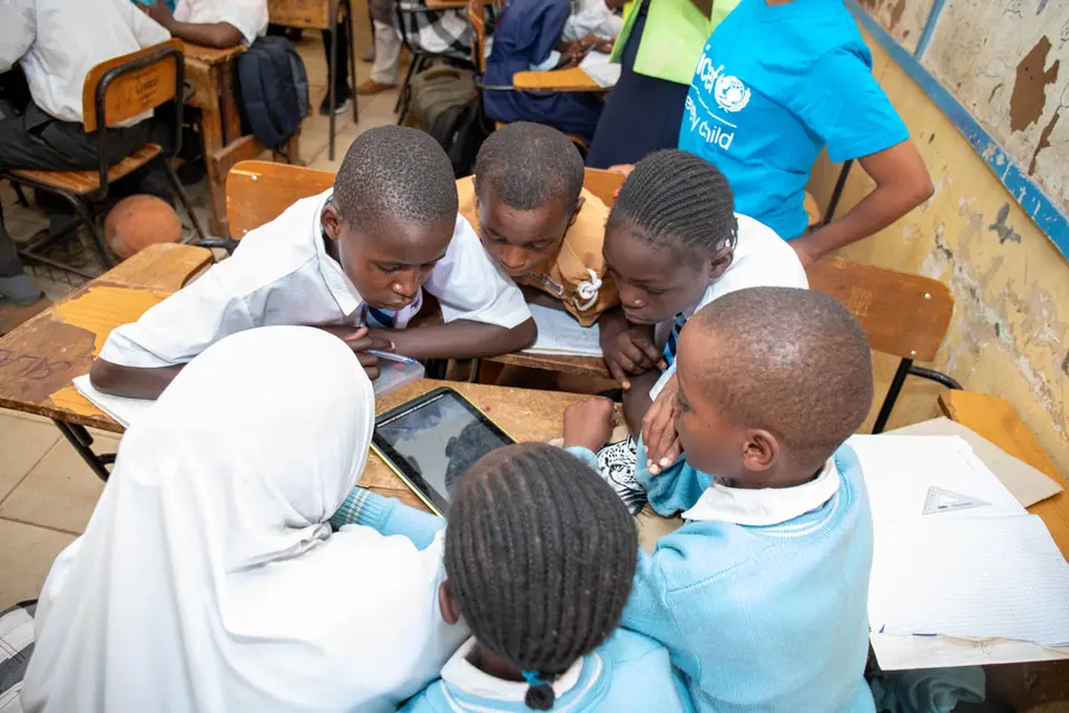 Children gathered around a digital learning tablet