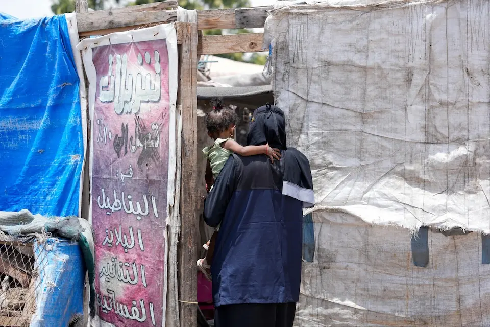 A community health volunteer enters a tent at a displacement camp in Yemen where she will conduct a home health visit.