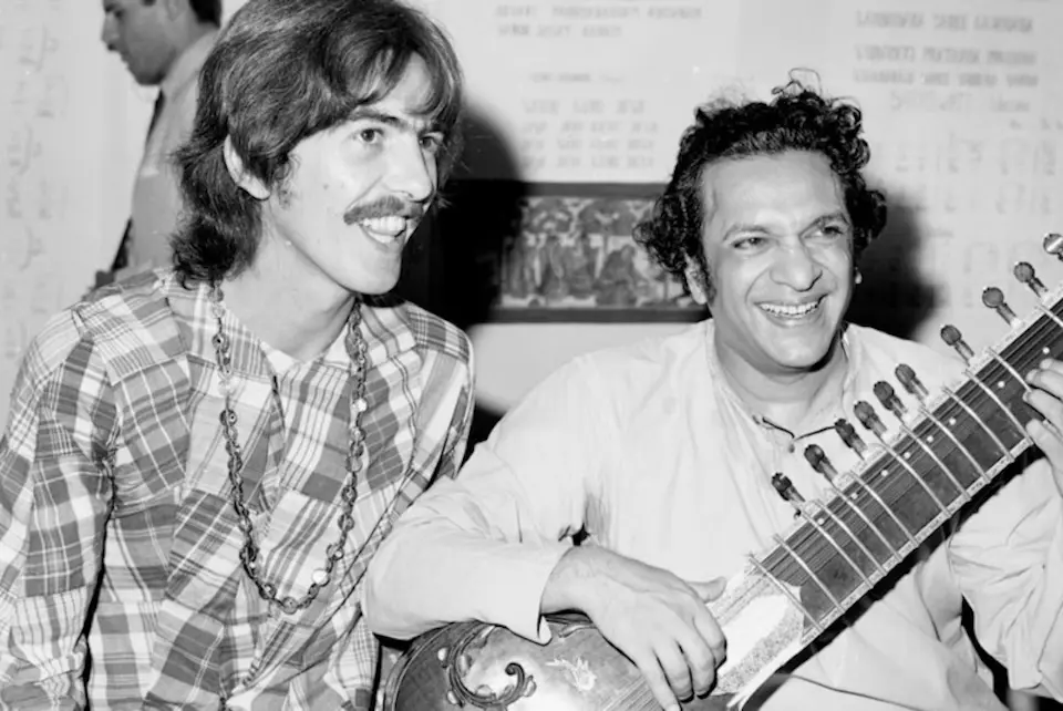 Black and white photo of George Harrison and Ravi Shankar, who is holding a sitar