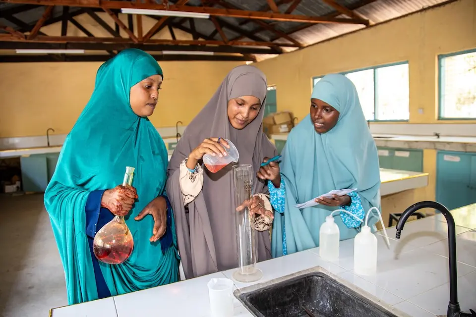 Three teenage girls participate in a science class at a refugee camp in Kenya.