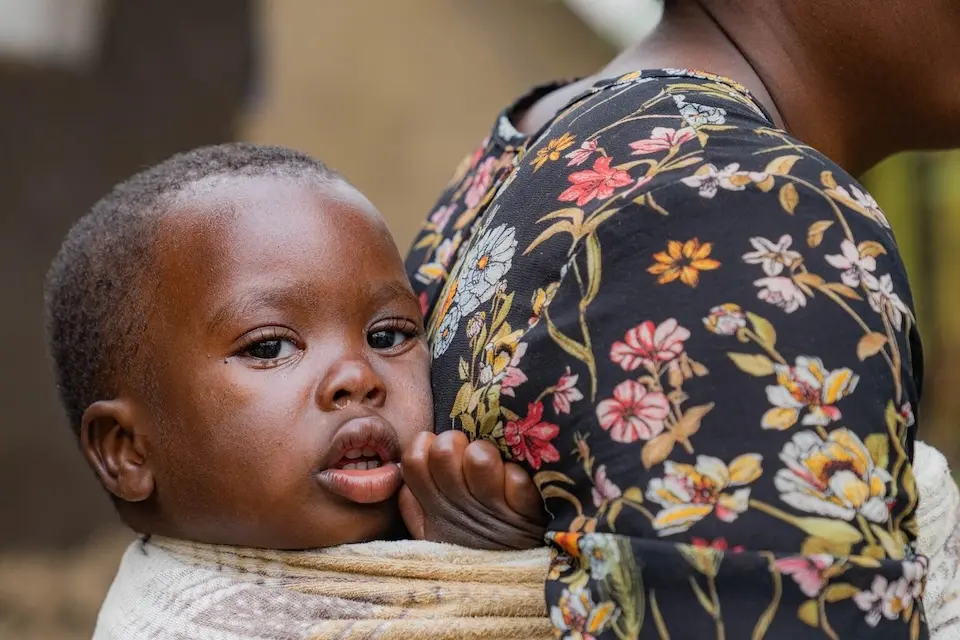 A mother in DR Congo displaced by conflict carries her baby on her back.