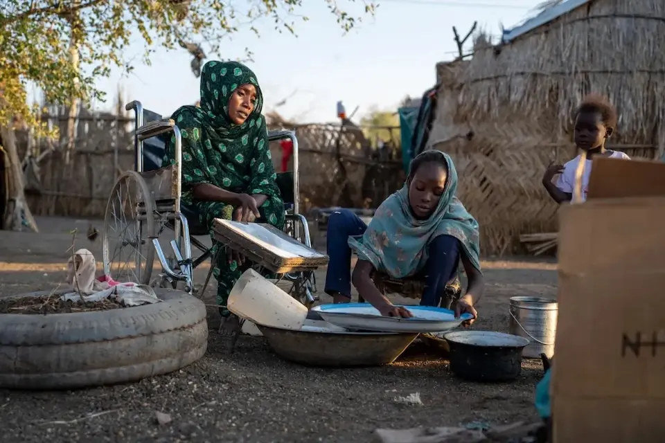 A mother in a wheelchair and one of her daughters do dishes in rural Gedaref, Sudan.