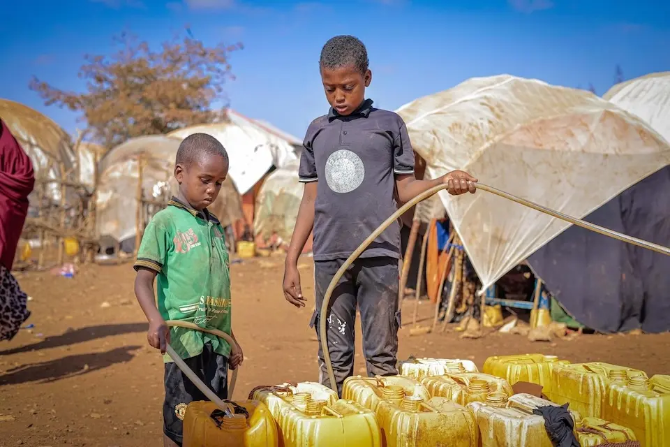 In Somalia, one boy holds a hose while another boy fills a jerry can of safe water at a UNICEF access point.