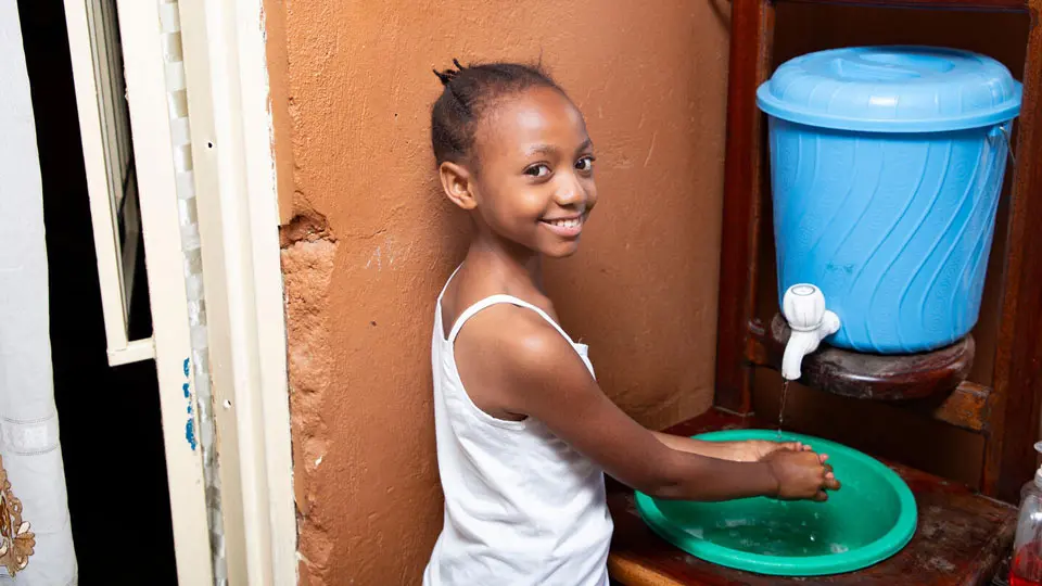 Young girl smiling and looking at the camera while washing her hands in a basin